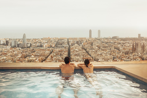 Couple relaxing on hotel rooftop looking at Barcelona city skyline. Photo composition.