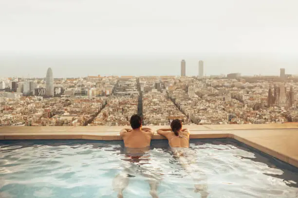 Photo of Couple relaxing on hotel rooftop looking at Barcelona city skyline. Photo composition.