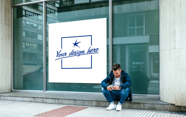 Customizable poster with a guy sitting looking mobile Customizable poster in a shop window with a guy sitting on the curb looking at the mobile outdoors store window stock pictures, royalty-free photos & images