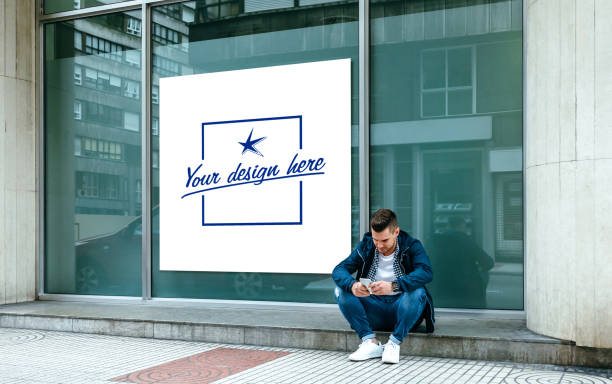 Customizable poster with a guy sitting looking mobile Customizable poster in a shop window with a guy sitting on the curb looking at the mobile outdoors shop window stock pictures, royalty-free photos & images