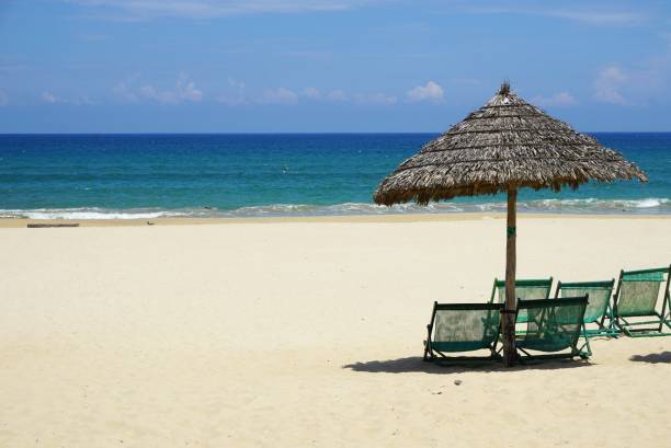 istock Thatched umbrella and chairs on a sunny sandy beach in Southeast Asia 1053013512