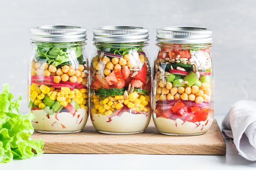 Three glass jars with layering various vegan salads for healthy lunch. The concept of fitness and vegetarian food.