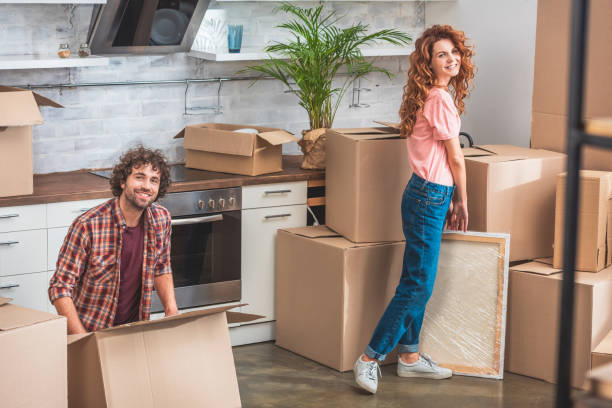 istock smiling couple unpacking cardboard boxes at new home and looking at camera 1053024900