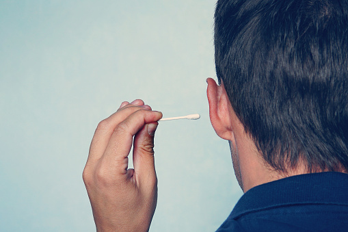 Happy man cleans his ear with a cotton swab close-up on blue background