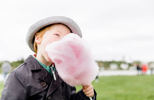 Young boy eating cotton candy Young boy enjoying eating a pink cotton candy. He is standing outdoors and wearing a hat. His face is hidden behind a pink sugar cloud. child cotton candy stock pictures, royalty-free photos & images