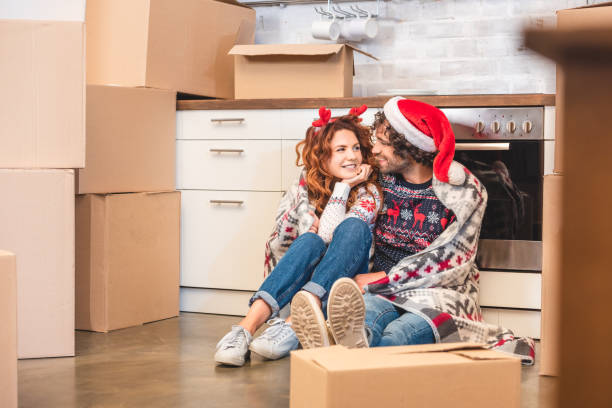happy young couple smiling each other while sitting between cardboard boxes at christmastime stock photo