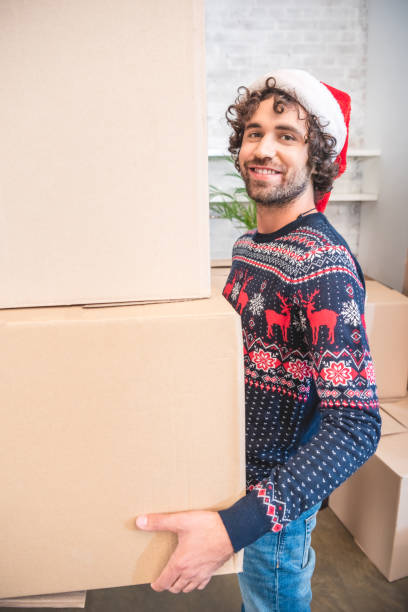istock happy young man in santa hat holding cardboard boxes and smiling at camera 1053036870