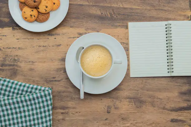 cappuccino in the white cup on wooden table and notebook and cookies