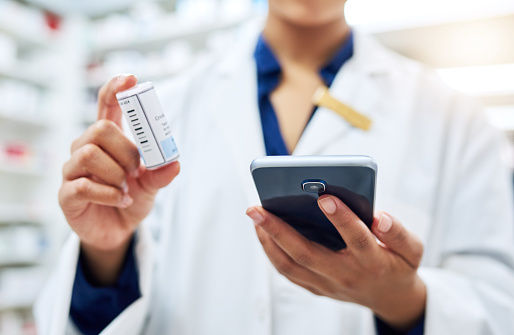 Cropped shot of a pharmacist using her cellphone while holding medication