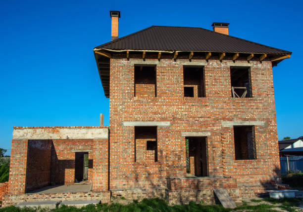 istock Unfinished brick house with holes for windows and doors under clear blue sky, still under construction 1053051444