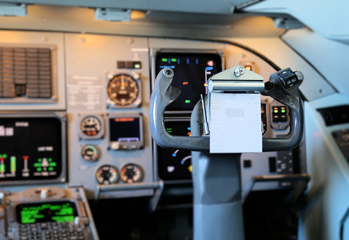 View inside the cockpit (flight deck) of a commercial jet aircraft showing the first officer's control column (also known as the yoke) with flight notes, plus instruments in the background