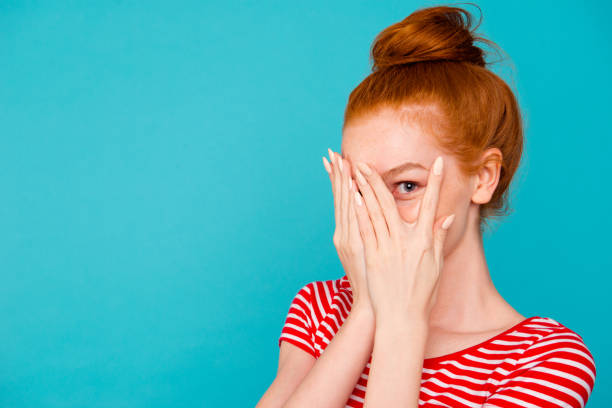 portrait of nice cute attractive magnificent lovely cheerful red-haired girl with bun,hiding face behind fingers, peeking, empty place, copy space, isolated on bright vivid blue background - hair bun hairstyle beautiful looking imagens e fotografias de stock