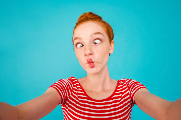 Self-portrait of crazy foolish playful pretty ecstatic cheerful red-haired girl with bun, grimacing, isolated on bright vivid blue background Self-portrait of crazy foolish playful pretty ecstatic cheerful red-haired girl with bun, grimacing, isolated on bright vivid blue background grimacing stock pictures, royalty-free photos & images