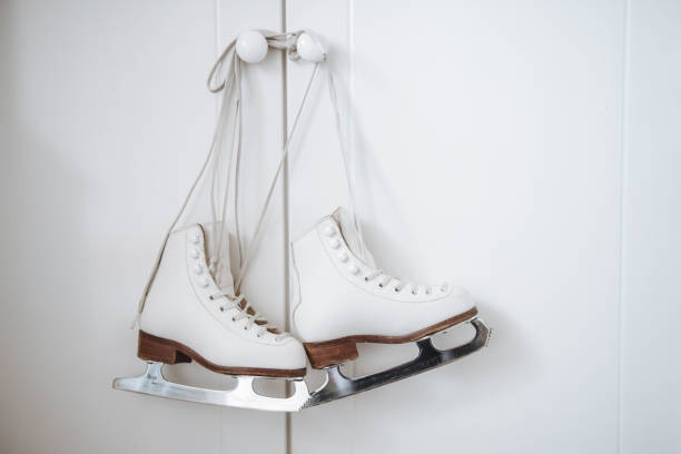 Two white figure skates with silver blades hanging on the hook on the wooden brown wardrobe, preparing for winter sports indoors, wallpaper, background