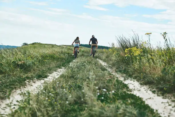 Happy couple riding bicycle outdoors at summer from back. A man and a woman are wearing a T-shirt and shorts are riding bicycles in a field.