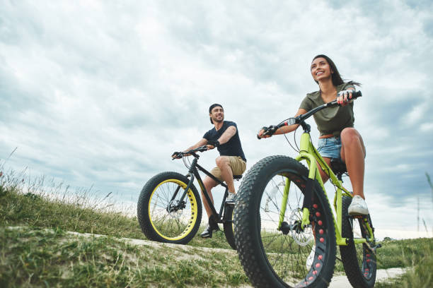 Young couple are cyclingat green hills . Front view