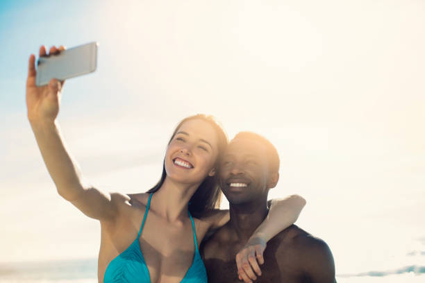 istock Smiling multi-ethnic couple taking selfie at beach 1053081864