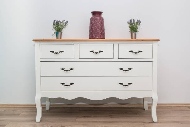 White wooden dresser with three vases and flowers on white wall background. Chest of drawers close up. White wooden dresser with three vases and flowers on white wall background. Chest of drawers close up. dresser stock pictures, royalty-free photos & images
