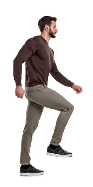 Photo of An isolated bearded man in casual wear steps up with one leg in a side view on a white background.