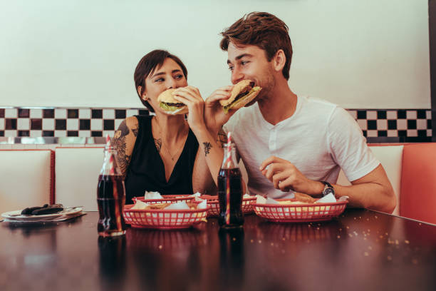 mężczyzna i kobieta jedzący hamburgery w restauracji - diner food zdjęcia i obrazy z banku zdjęć