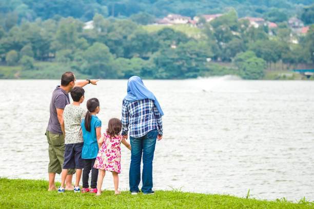 A muslim father spot something opposite the lakeside and try to show to his family. They are planning to go there and have a look.