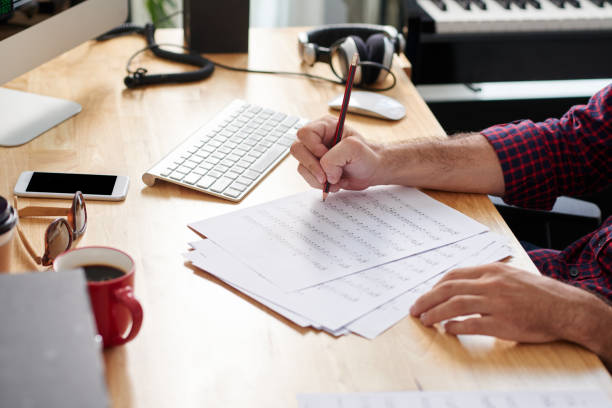Close-up of composer sitting at the table with sheets of paper and composing music