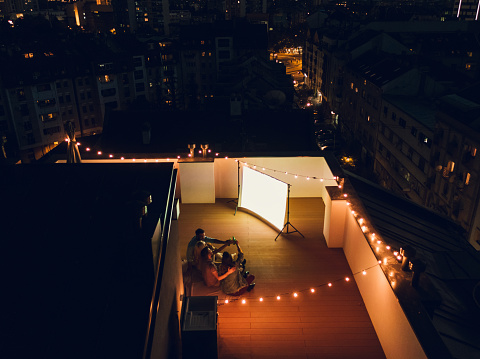 Aerial shot of four friends hanging out and watching movie on a rooftop