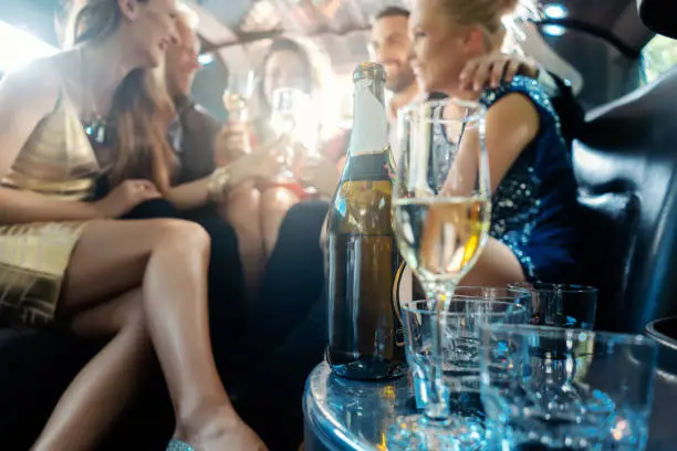 Women and men celebrating with drinks in a limousine car, focus on the alcohol bottle