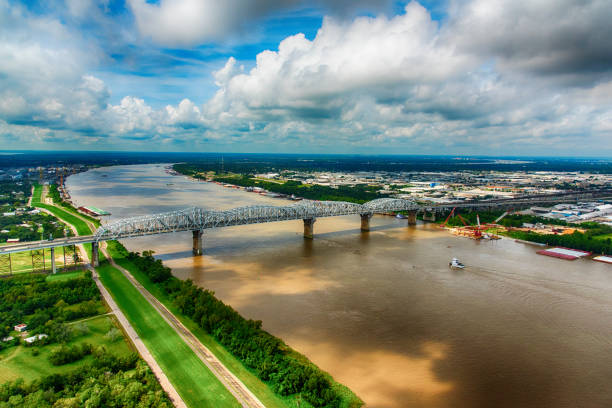 Bridge Over The Southern Mississippi A tug boat moving toward a bridge spanning the mighty Mississippi River in southern Louisiana near New Orleans. bridge crossing cloud built structure stock pictures, royalty-free photos & images