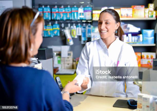 Photo libre de droit de Souriant Pharmacien Séduisante Jeune Rousse Remettre Les Médicaments Prescrits À Une Patiente Âgée Vue Sur Lépaule De Clients Du Pharmacien banque d'images et plus d'images libres de droit de Pharmacie