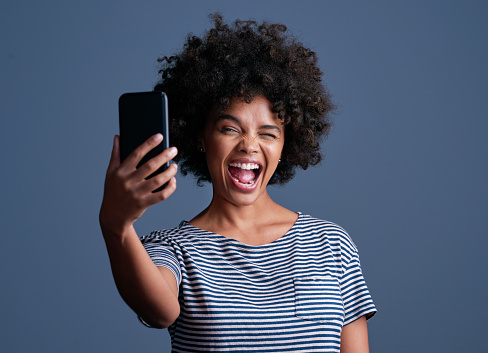 Studio shot of an attractive young woman taking a selfie on a mobile phone against a blue background
