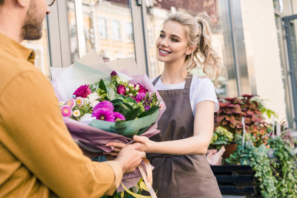 улыбающийся флорист дает красивый букет хризантем для клиента возле цветочного магазина - store flower bouquet florist стоковые фото и изображения