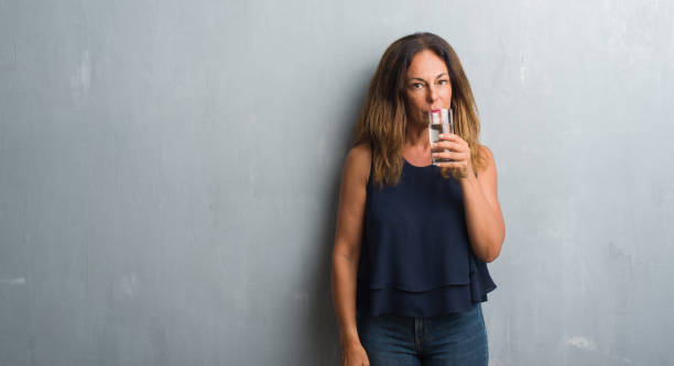 istock Middle age hispanic woman drinking glass of water with a confident expression on smart face thinking serious 1053158384