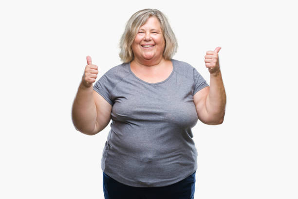 シニア プラスのサイズの白人女性の手で肯定的なジェスチャーを行う分離背景成功記号の上の親指を笑顔と幸せ。勝者ジェスチャー晴れやかな表情でカメラを見てください。 - senior women cheerful overweight smiling ストックフォトと画像