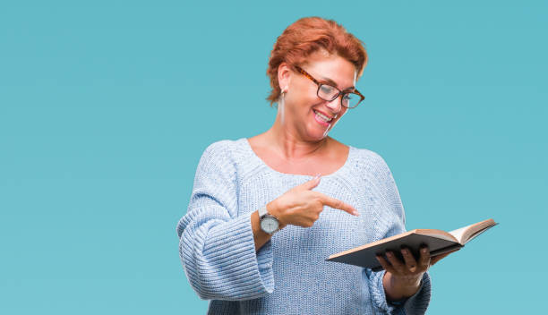 senior caucasian woman reading a book over isolated background very happy pointing with hand and finger - women professor mature adult human face imagens e fotografias de stock