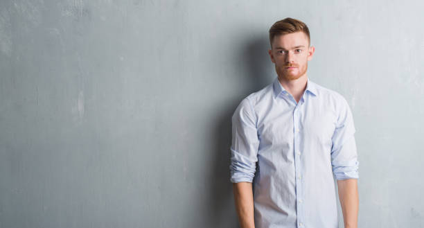 istock Young redhead business man over grey grunge wall with serious expression on face. Simple and natural looking at the camera. 1053172876