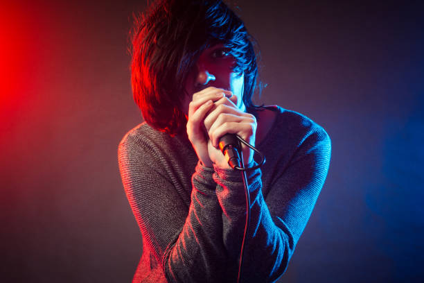 singing singer on concert The young singer or vocalist in emo style is singing on concert on background of red and blue concert lights. emo boy stock pictures, royalty-free photos & images