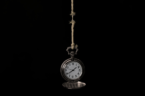 Pocket watch hanging with frayed rope on black background. Time pressure.