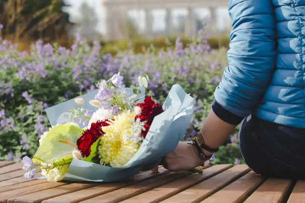 A bouquet of flowers on a bench in the autumn park as a concept of waiting for a romantic meeting.