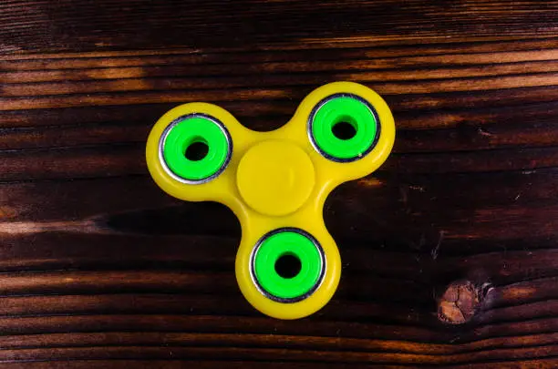 Photo of Yellow fidget spinner on wooden desk. Top view
