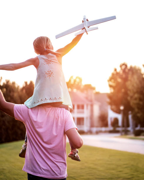 Daughter on Shoulders of Father in Park Little girl holding model airplane sitting on shoulders of father in park. toy airplane stock pictures, royalty-free photos & images