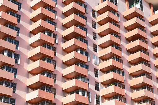 Abstract pattern view on residential, apartment complex building with many windows, balconies painted in pink, orange during sunny day