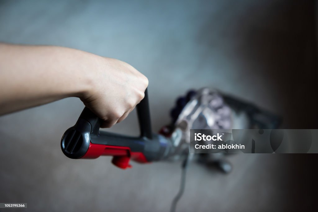 Closeup, high angle, above, looking down view of hand holding handle of vacuum cleaner cleaning room carpet floor Vacuum Cleaner Stock Photo