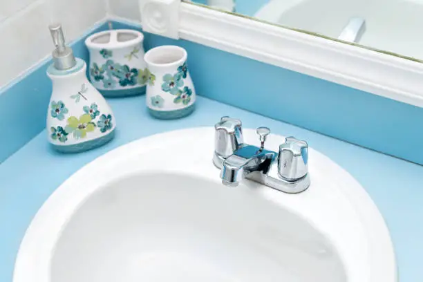 Closeup view above of blue, teal, turquoise modern, paint, painted bathroom tiled walls, mirror, sink, water faucet with liquid soap dispensers, vanity