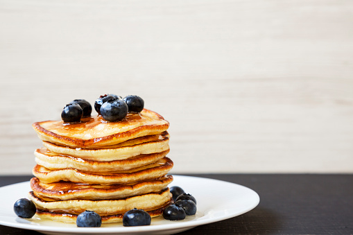 Pancakes with blueberries and honey on a white round plate, side view. Copy space.