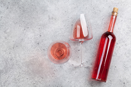 Rose wine bottle and glass lying on stone backdrop. Top view with space for your text