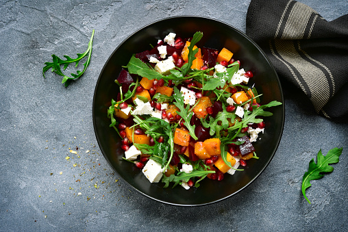 Pumpkin salad with beetroot, arugula and feta cheese in a black bowl over dark grey slate, stone or concrete background.Top view.