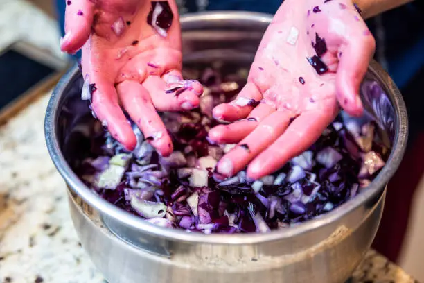 Woman, female hands, palms after mixing, massaging red, purple cabbage, onion raw vegan, vegetarian salad in stainless steel, metal bown, plate, dish in kitchen granite countertop