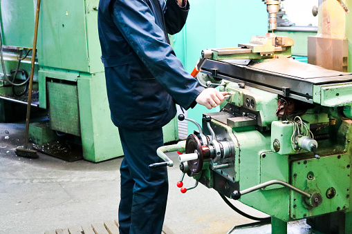 A male worker works on a larger metal iron locksmith lathe, equipment for repairs, metal work in a workshop at a metallurgical plant in a repair production.