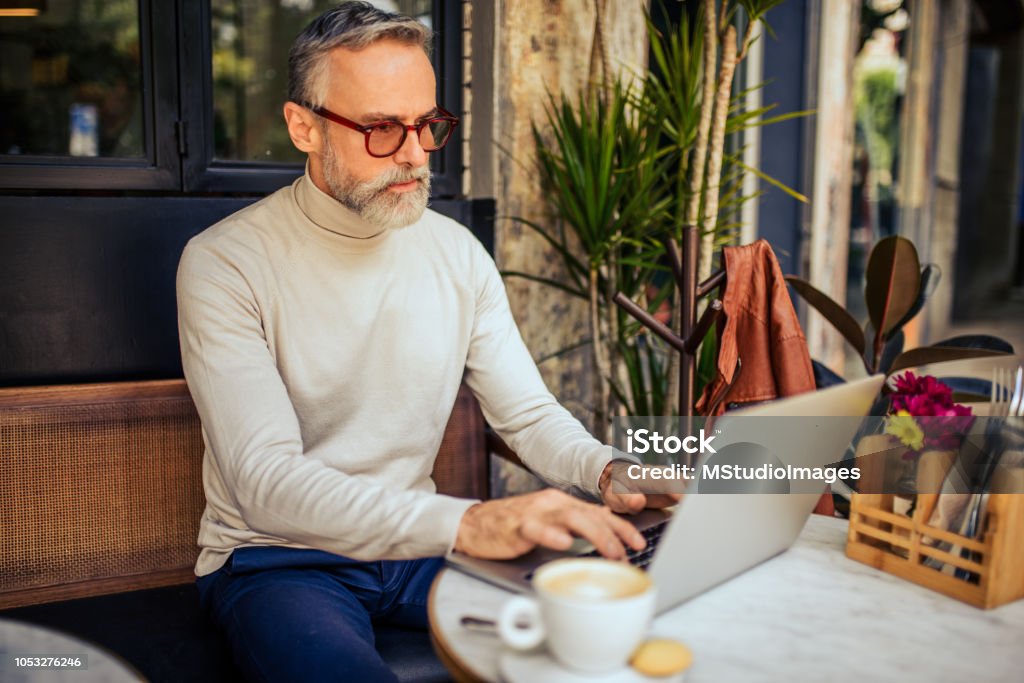 Working from the bar. Handsome mature adult using laptop at the bar. He has positive emotion while drinking coffee Bar - Drink Establishment Stock Photo